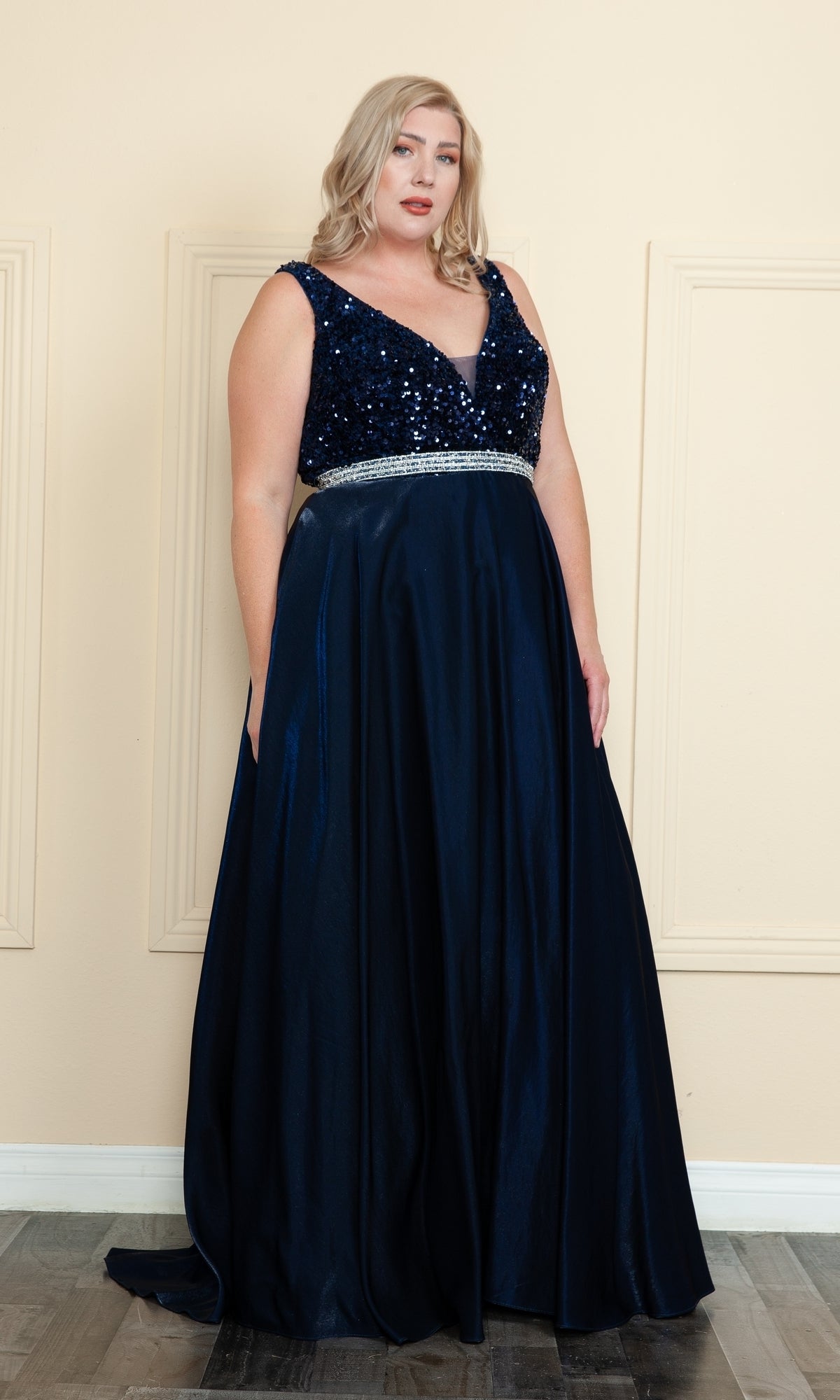 A woman in a navy Plus-Size Long Sequin-Bodice Prom Dress W1006 stands indoors against a beige wall.